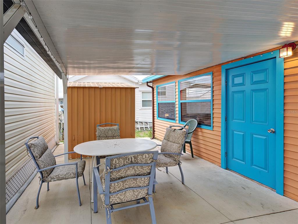 A covered patio features a dining table with four chairs and a bright blue door — 1475 FLAMINGO DRIVE UNIT 286, ENGLEWOOD, FL