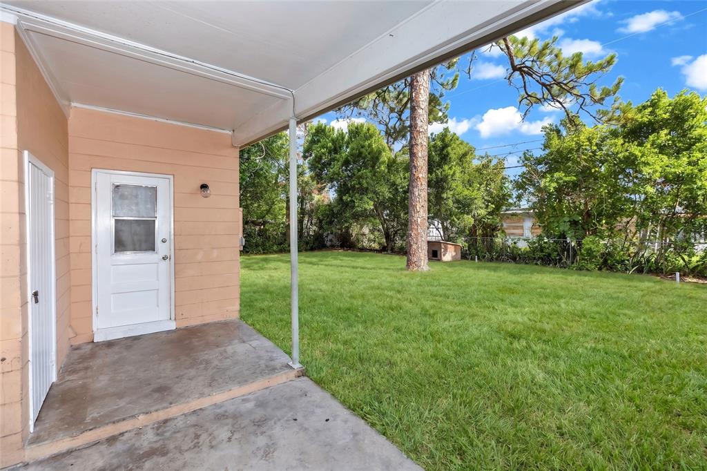 A concrete patio with a white door overlooks a grassy backyard with a dog house — 1106 MYRTLE LANE, COCOA, FL