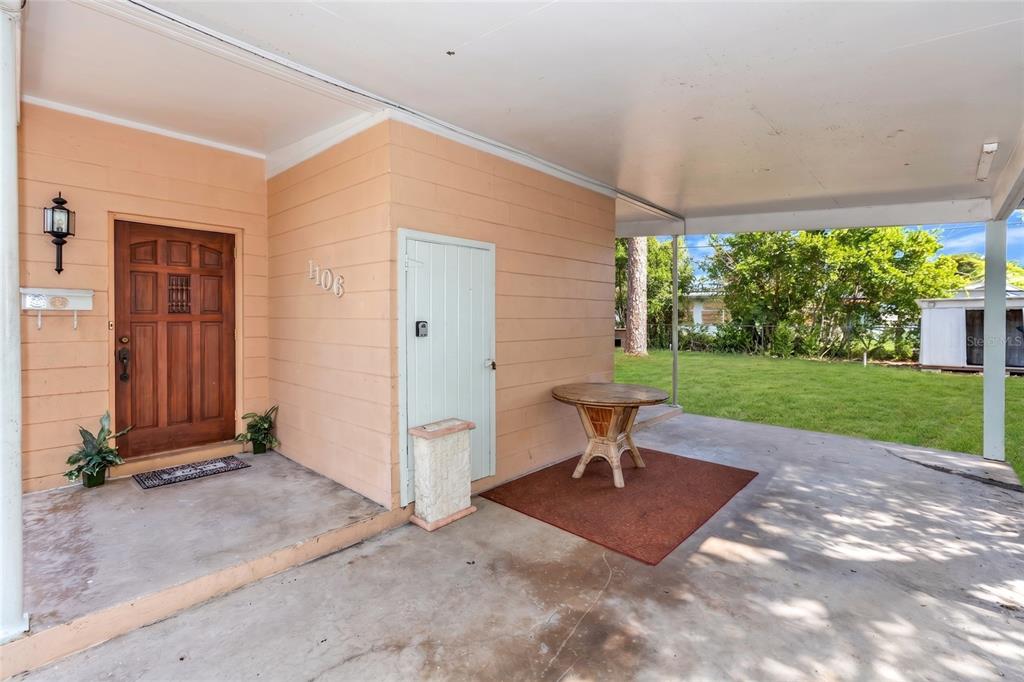 A covered concrete patio features a wooden front door, a storage closet, and a small table — 1106 MYRTLE LANE, COCOA, FL