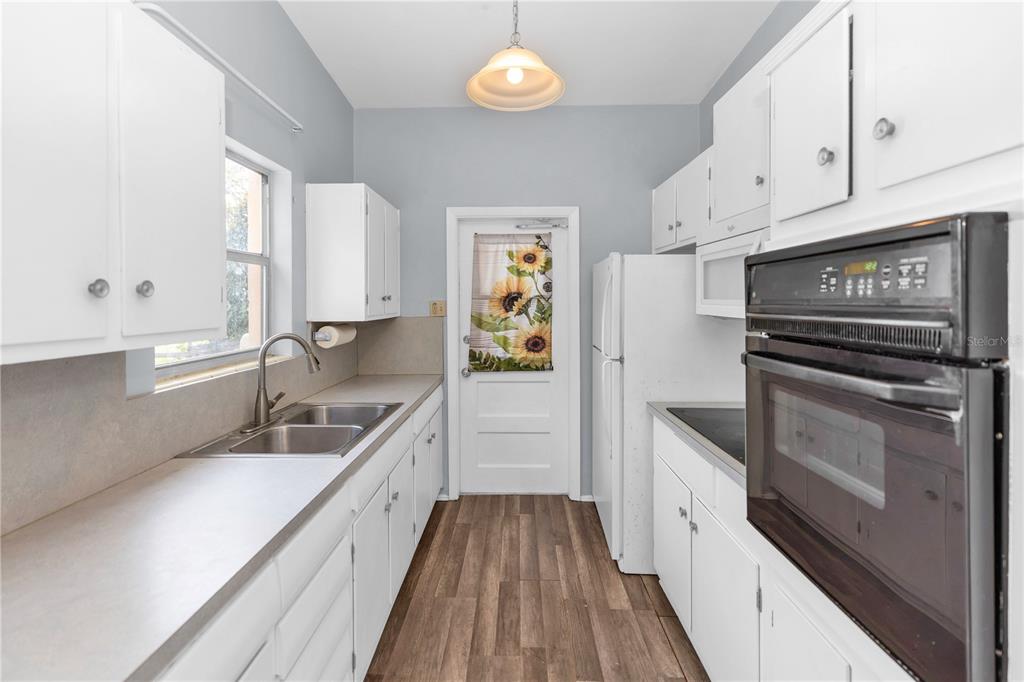 A galley kitchen features white cabinets, a double sink, wood-look flooring, and a wall oven — 1106 MYRTLE LANE, COCOA, FL