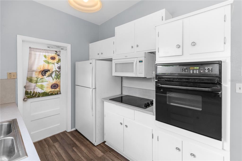 A kitchen features white cabinets, a black wall oven, a cooktop, and a white refrigerator — 1106 MYRTLE LANE, COCOA, FL