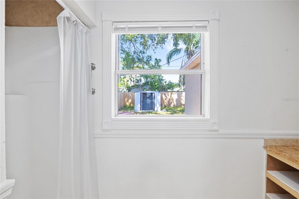 A bathroom features a white shower curtain, a window with white trim, and open shelving — 3005 W KATHLEEN STREET, TAMPA, FL