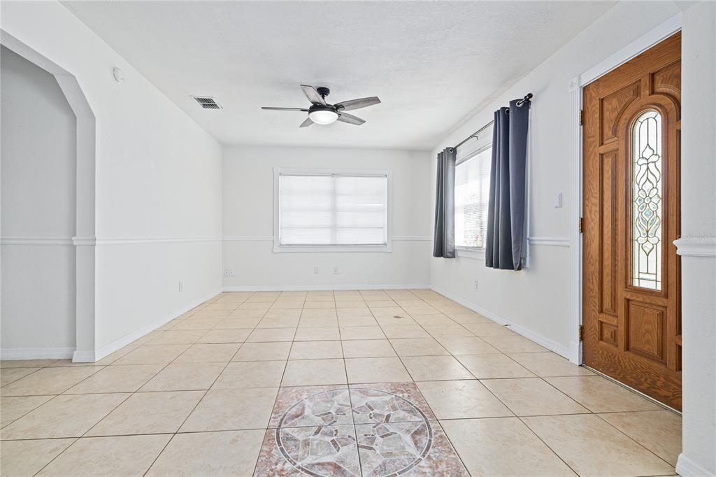 An empty room with beige tile flooring, a ceiling fan, and a wooden front door — 3005 W KATHLEEN STREET, TAMPA, FL