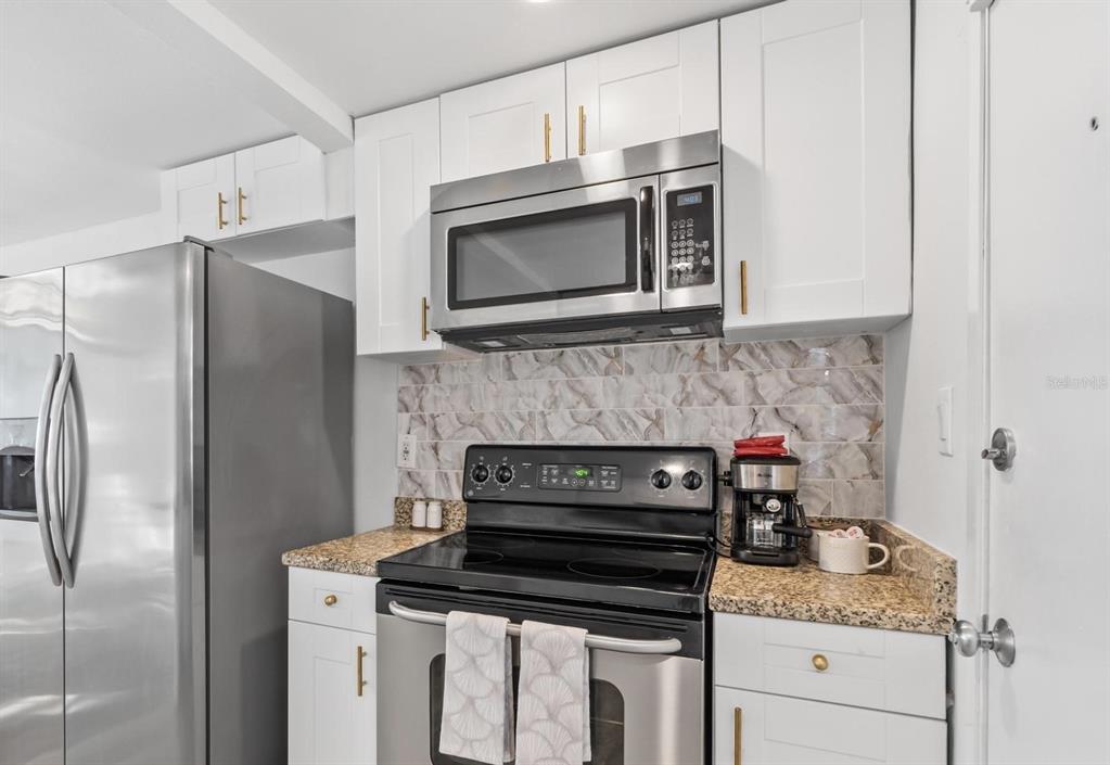 A kitchen features white cabinets, stainless steel appliances, granite countertops, and a marble-patterned backsplash — 7799 46TH AVE N, ST PETERSBURG, FL