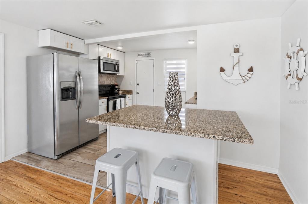 A kitchen features a granite-topped island, stainless steel appliances, and nautical wall decor — 7799 46TH AVE N, ST PETERSBURG, FL