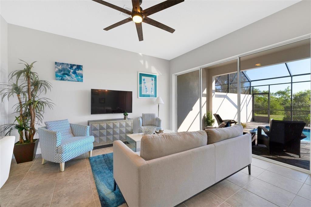 A living room features a sofa, patterned armchairs, a television, and sliding doors to a pool — 490 CAPTIVA DRIVE, DAVENPORT, FL