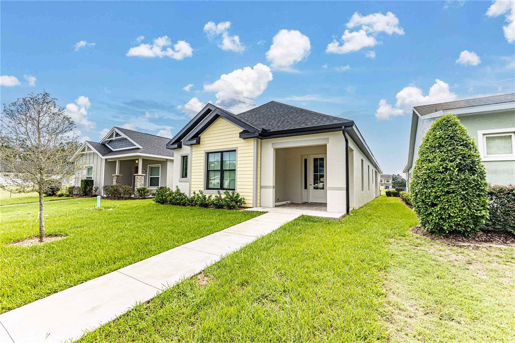 A yellow single-story house with a front walkway and a covered entryway under a blue sky — 10619 GRAND OAKS BOULEVARD, OXFORD, FL