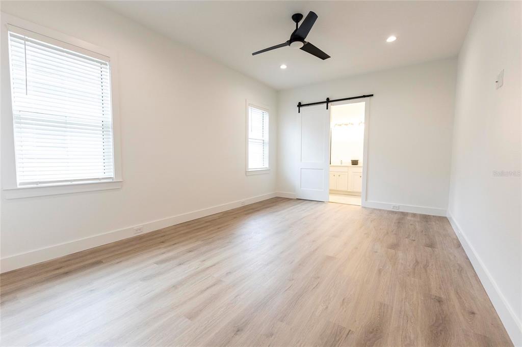 A bedroom with light wood-look flooring, white walls, a ceiling fan, and a sliding barn door — 10619 GRAND OAKS BOULEVARD, OXFORD, FL