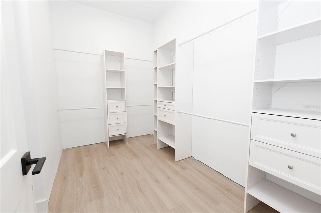 A walk-in closet features white shelving units, drawers, and light wood-look flooring — 10619 GRAND OAKS BOULEVARD, OXFORD, FL