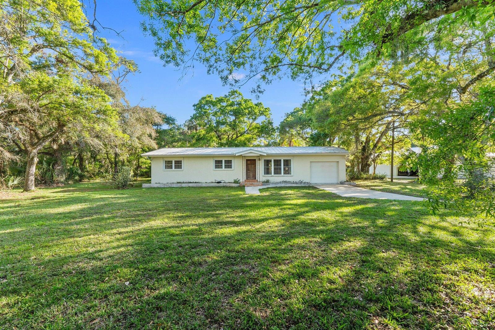 A single-story house with a metal roof and attached garage sits on a grassy lot — 11541 Okeechobee Road, Fort Pierce FL 34945, FORT PIERCE, FL