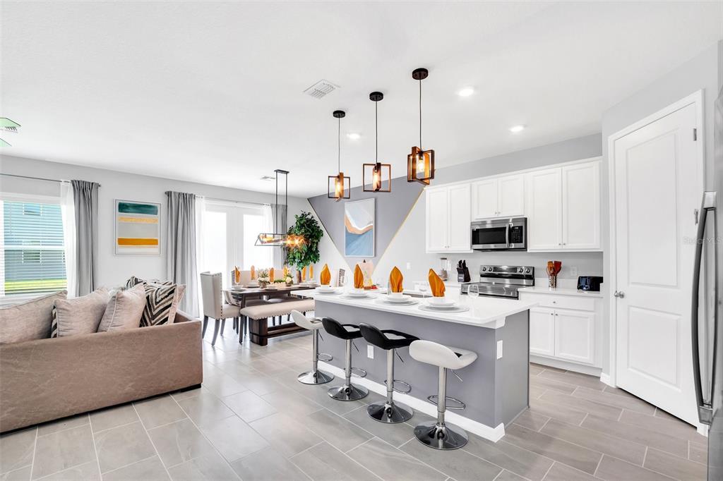 A modern open-concept kitchen and dining area features white cabinetry, a gray island, and pendant lighting — 2131 DERWENT DRIVE, DAVENPORT, FL