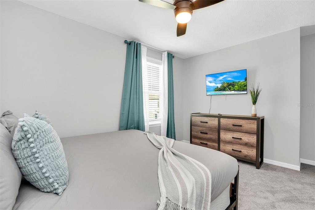 A bedroom features a bed with grey bedding, a wooden dresser, and a wall-mounted television — 2131 DERWENT DRIVE, DAVENPORT, FL