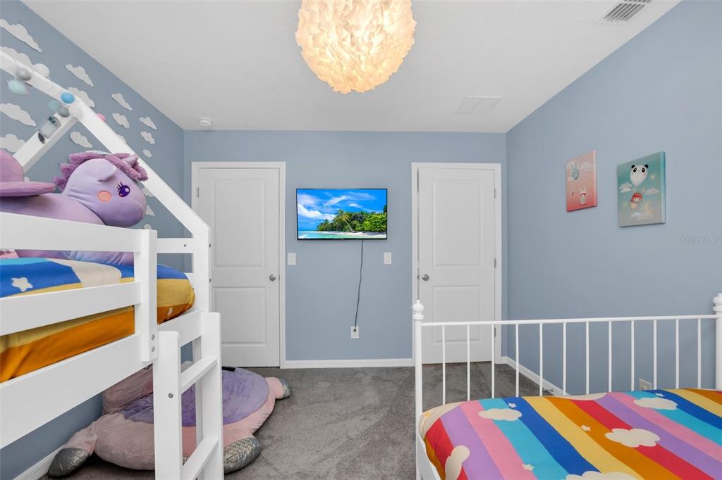 A bedroom with blue walls, two white beds, a wall-mounted television, and gray carpeting — 2131 DERWENT DRIVE, DAVENPORT, FL