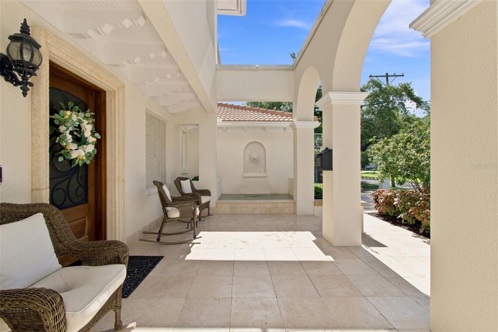 A covered stone patio features arched columns, wicker rocking chairs, and a wall fountain — 4537 W SWANN AVENUE, TAMPA, FL