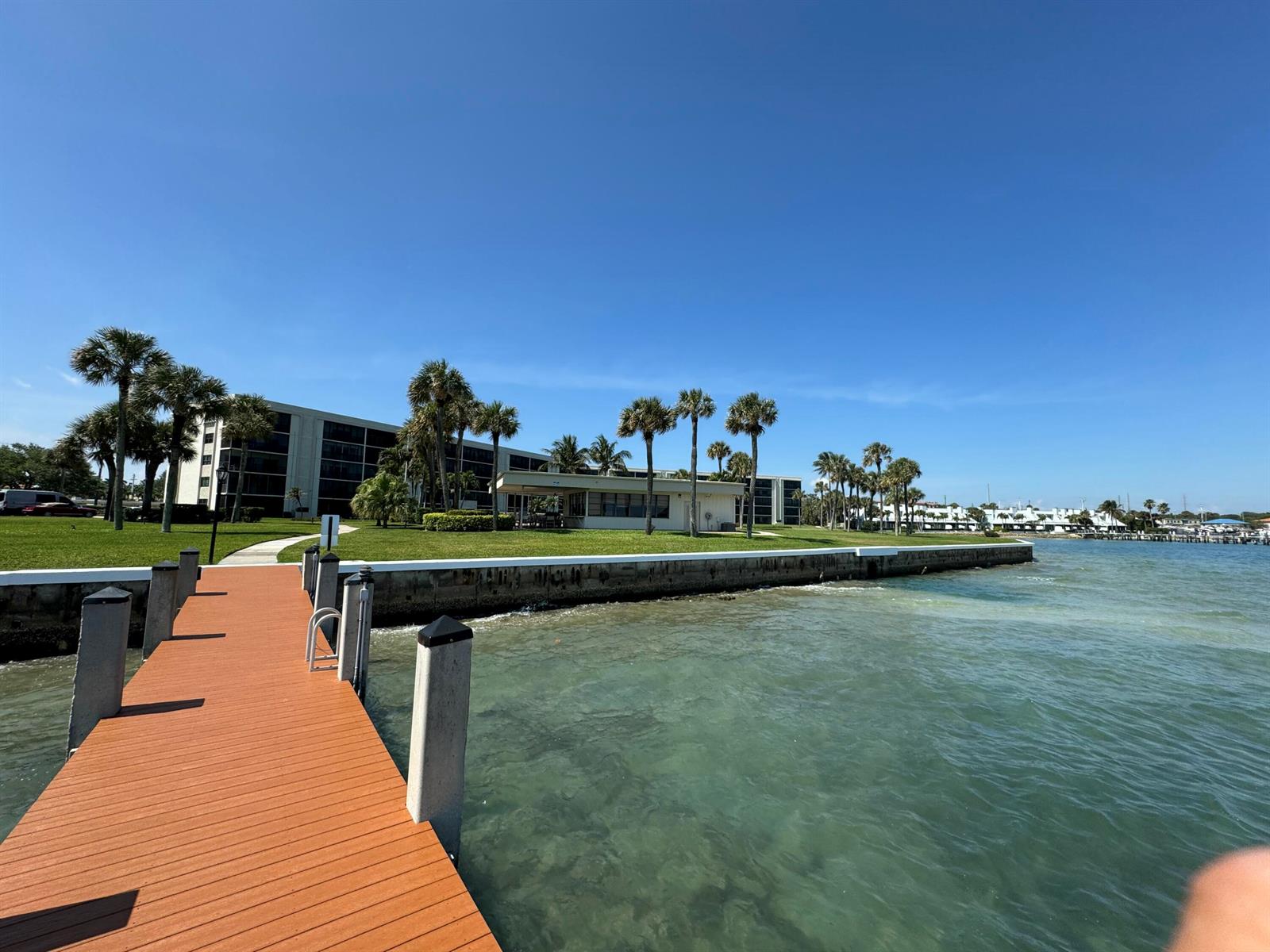 A wooden dock extends into clear water toward a waterfront building with palm trees — 200 Intracoastal Place # 404, Jupiter FL 33469, JUPITER, FL