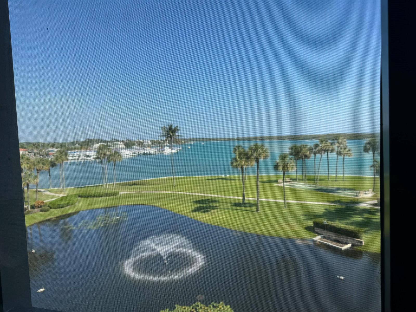 A view from a window overlooking a pond with a fountain, lawn, and distant bay — 200 Intracoastal Place # 404, Jupiter FL 33469, JUPITER, FL