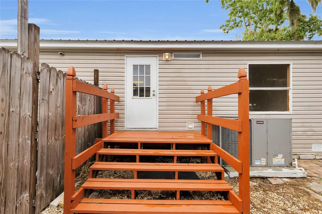 A wooden staircase leads to a white door on the exterior of a beige house — 16 CAYMAN CIRCLE, UMATILLA, FL