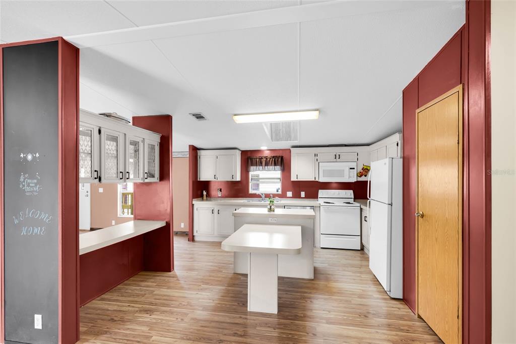 A kitchen features white cabinets, a central island, and red walls with wood-look flooring — 16 CAYMAN CIRCLE, UMATILLA, FL