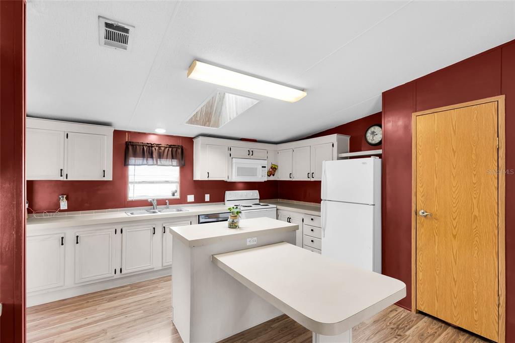 A kitchen features white cabinets, a central island with an attached table, and red walls — 16 CAYMAN CIRCLE, UMATILLA, FL