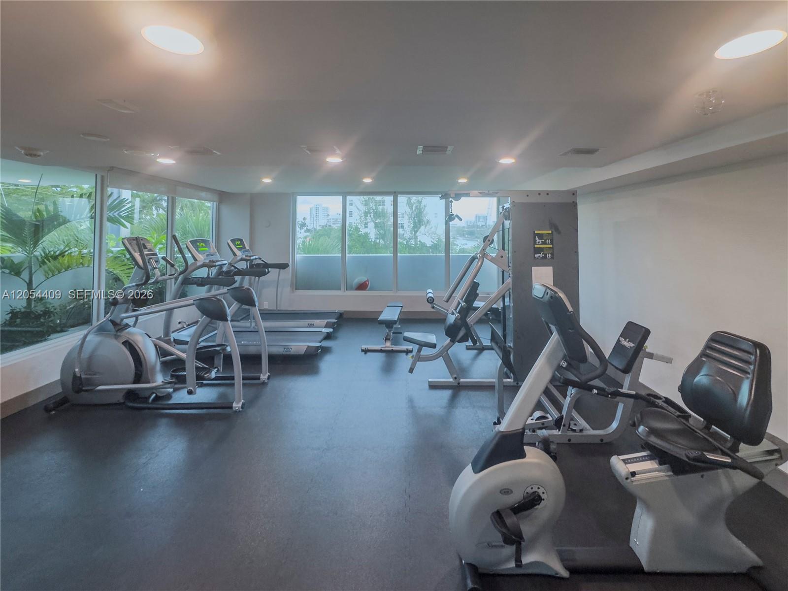 This gym features various exercise machines, rubber flooring, and large windows overlooking the outdoors — 9261 E Bay Harbor Dr # 405, Bay Harbor Islands FL 33154, BAY HARBOR ISLANDS, FL