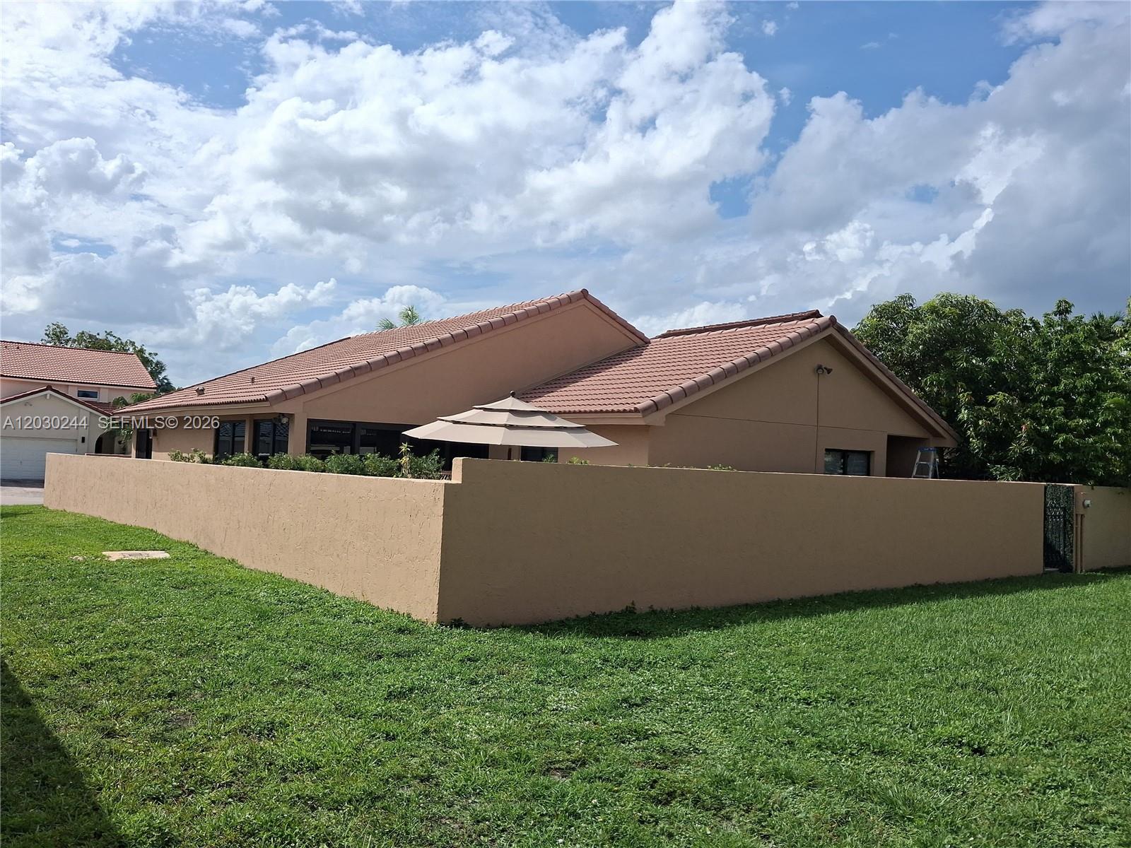 A tan house with a tiled roof is enclosed by a matching stucco perimeter wall — 17531 NW 62nd Pl N, Hialeah FL 33015, HIALEAH, FL
