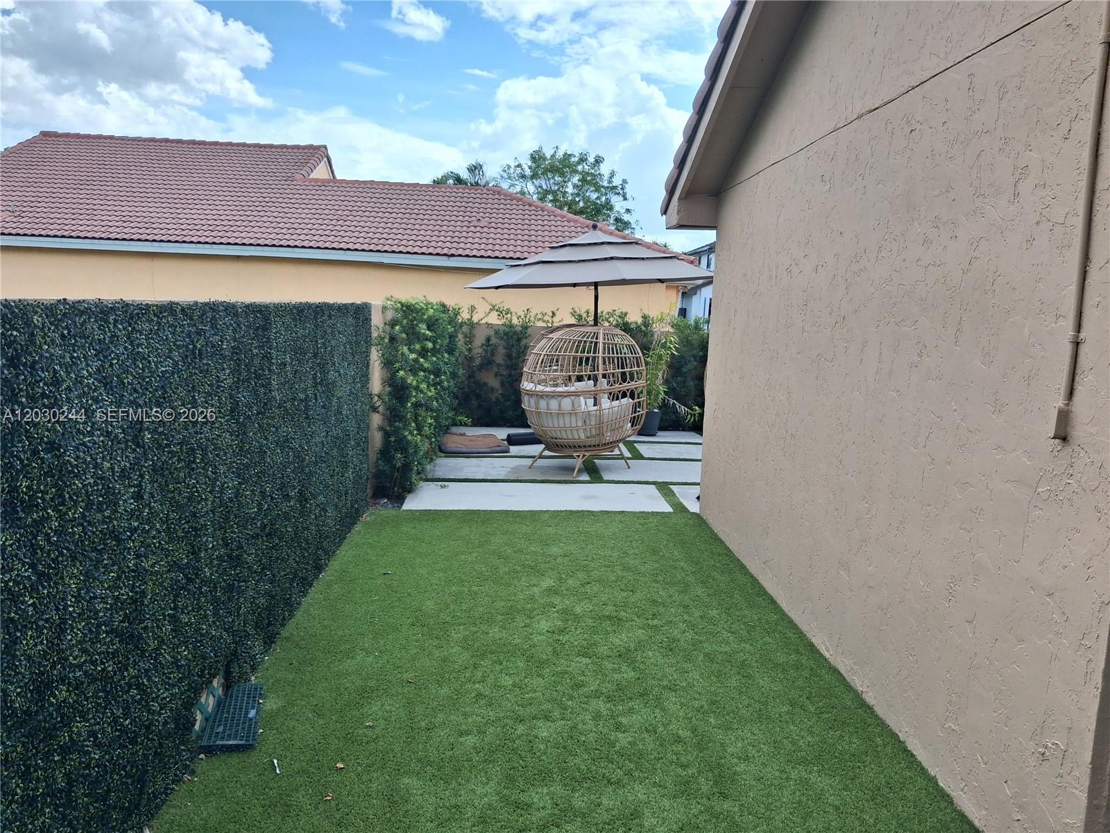 A small backyard features artificial turf, a privacy hedge, and a hanging egg chair — 17531 NW 62nd Pl N, Hialeah FL 33015, HIALEAH, FL
