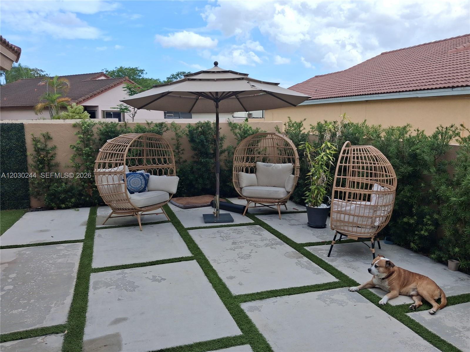 A patio features three wicker egg chairs, a large umbrella, and a dog on pavers — 17531 NW 62nd Pl N, Hialeah FL 33015, HIALEAH, FL
