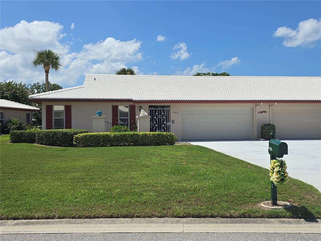 A single-story house with a white tile roof, a two-car garage, and a green lawn — 6601 11TH AVENUE W UNIT 6003, BRADENTON, FL