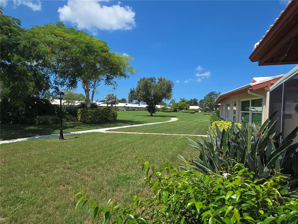 A grassy lawn with a winding walkway sits between residential buildings under a blue sky — 6601 11TH AVENUE W UNIT 6003, BRADENTON, FL