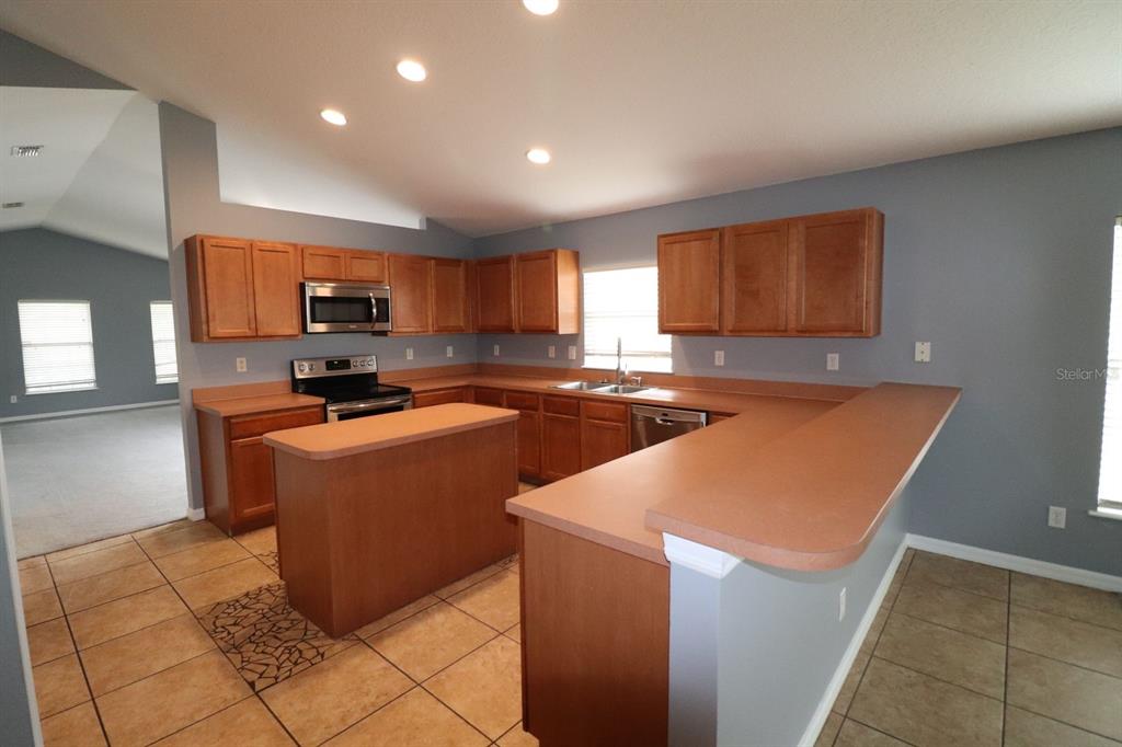 A kitchen features wood cabinets, brown laminate countertops, tile flooring, and stainless steel appliances — 324 RED KITE DRIVE, GROVELAND, FL