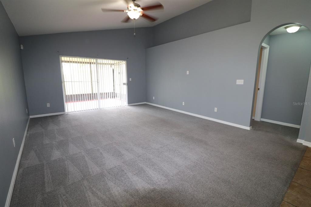 An empty living room features gray walls, gray carpeting, a ceiling fan, and sliding glass doors — 324 RED KITE DRIVE, GROVELAND, FL