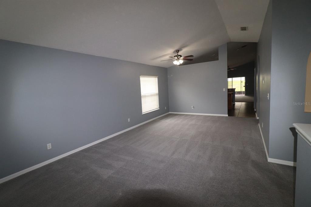 A spacious living room with gray walls, gray carpeting, and a ceiling fan — 324 RED KITE DRIVE, GROVELAND, FL