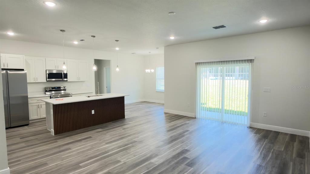 An open-concept kitchen and living area feature white cabinetry, a wood-paneled island, and gray flooring — 4522 SW 170TH STREET ROAD, OCALA, FL