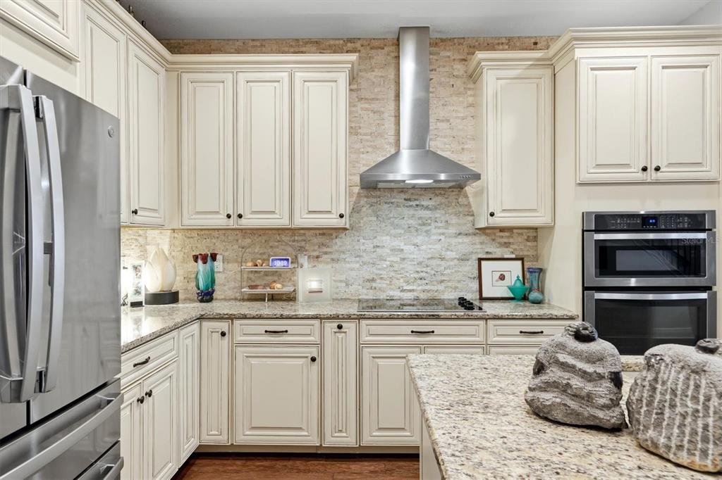 A kitchen features cream-colored cabinets, stainless steel appliances, granite countertops, and a stone tile backsplash — 3684 FESCUE LANE, SARASOTA, FL