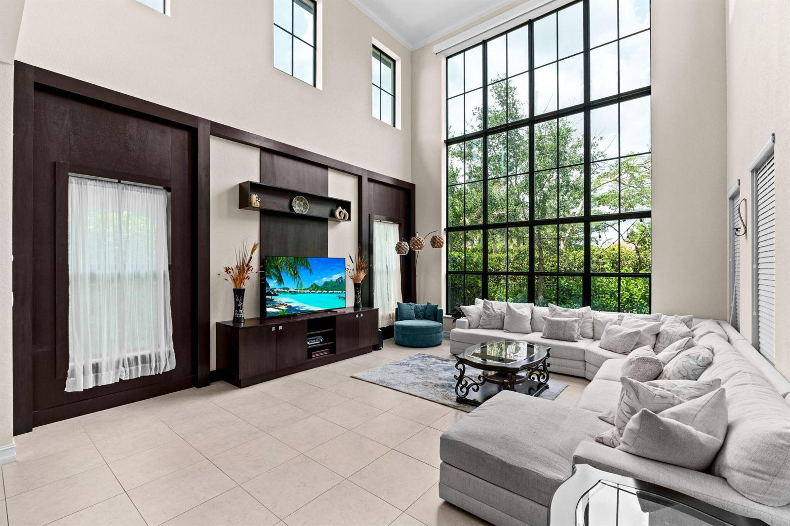 A living room features a double-height window wall, dark wood paneling, and a sectional sofa — 8845 WATERCREST Circle W, Parkland FL 33076, PARKLAND, FL