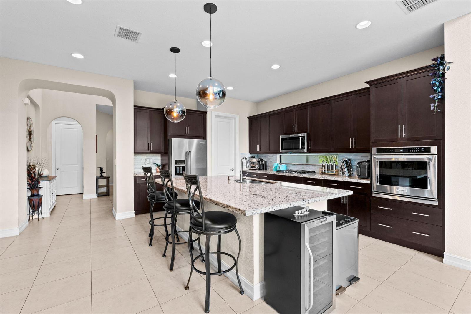 A kitchen features dark wood cabinets, granite countertops, a central island, and stainless steel appliances — 8845 WATERCREST Circle W, Parkland FL 33076, PARKLAND, FL