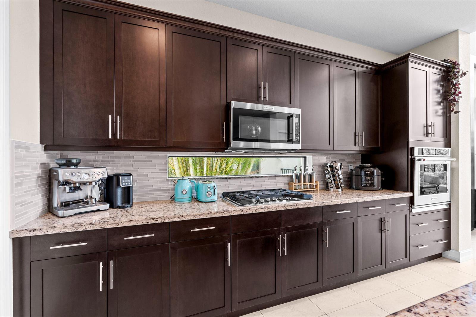 A kitchen features dark wood cabinets, granite countertops, a stainless steel microwave, and a backsplash — 8845 WATERCREST Circle W, Parkland FL 33076, PARKLAND, FL