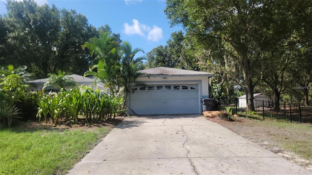 A concrete driveway leads to a one-car garage attached to a house with mature trees — 895 KEEN ROAD, FROSTPROOF, FL