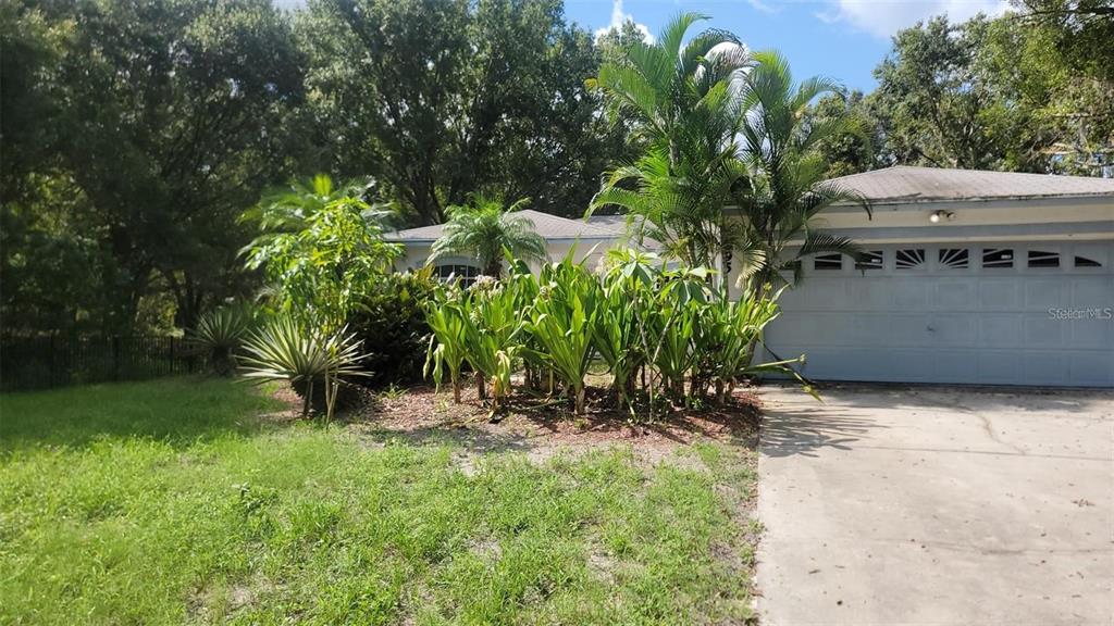 A single-story house with a light-colored exterior, a two-car garage, and lush tropical landscaping — 895 KEEN ROAD, FROSTPROOF, FL