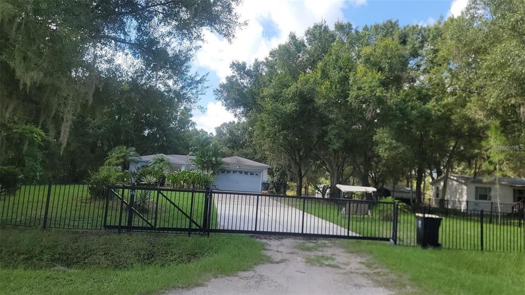 A gated driveway leads to a single-story house surrounded by mature trees and green lawn — 895 KEEN ROAD, FROSTPROOF, FL