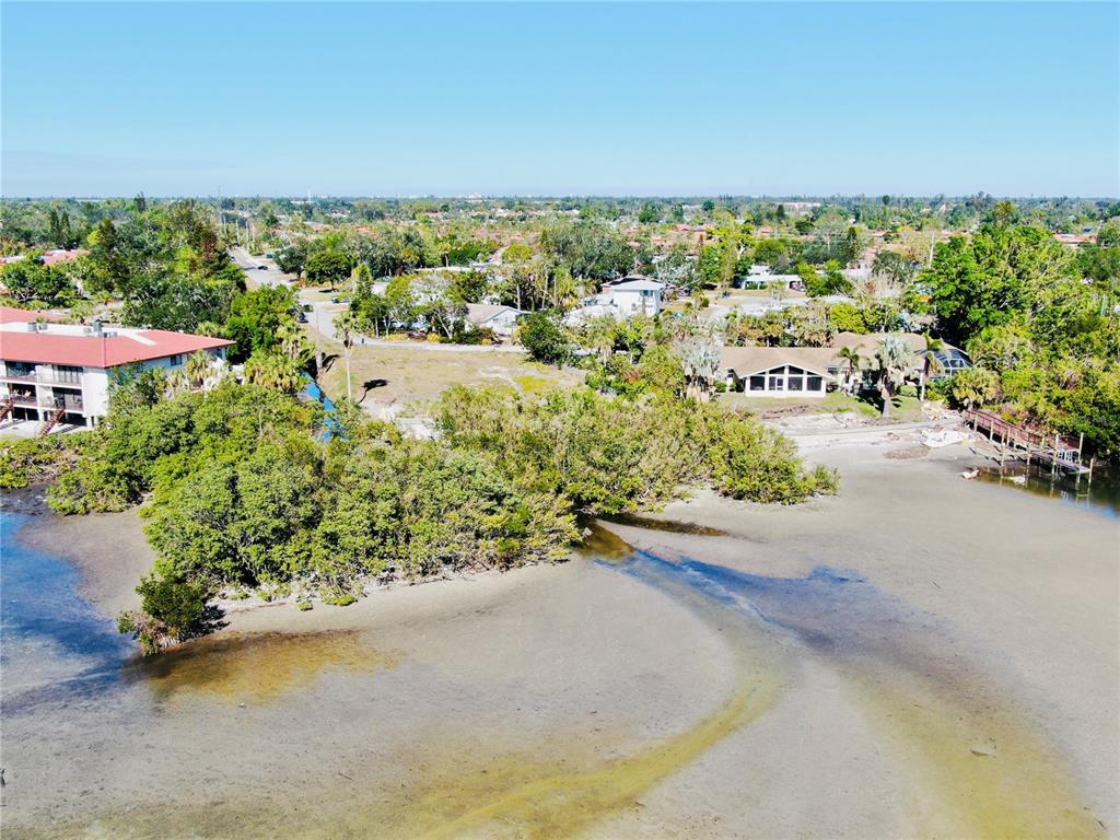 An aerial view shows a waterfront property with a house, vegetation, and a sandy shoreline — 6649 RENSSALAER DRIVE, BRADENTON, FL