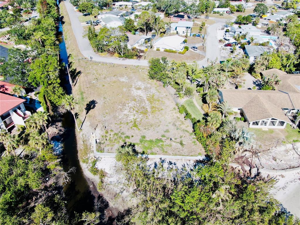 An aerial view shows a vacant, grassy residential lot bordered by a canal and trees — 6649 RENSSALAER DRIVE, BRADENTON, FL