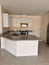 A kitchen features white cabinets, granite countertops, a kitchen island, and stainless steel appliances — 9282 WESTSIDE HILLS DRIVE, DAVENPORT, FL
