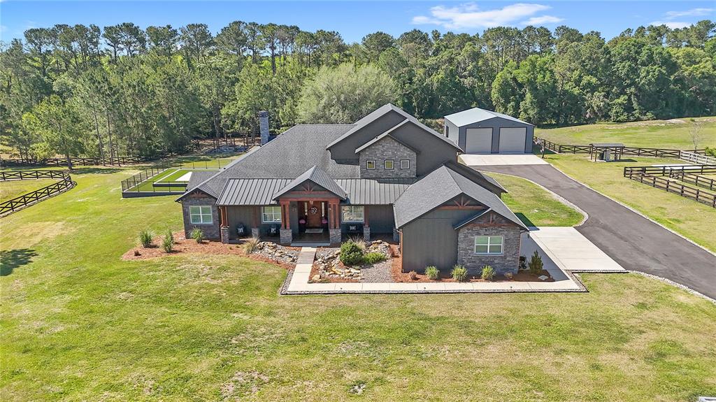 An aerial view shows a dark-sided house with a metal roof, stone accents, and garage — 22250 DEER PARK AVENUE, EUSTIS, FL
