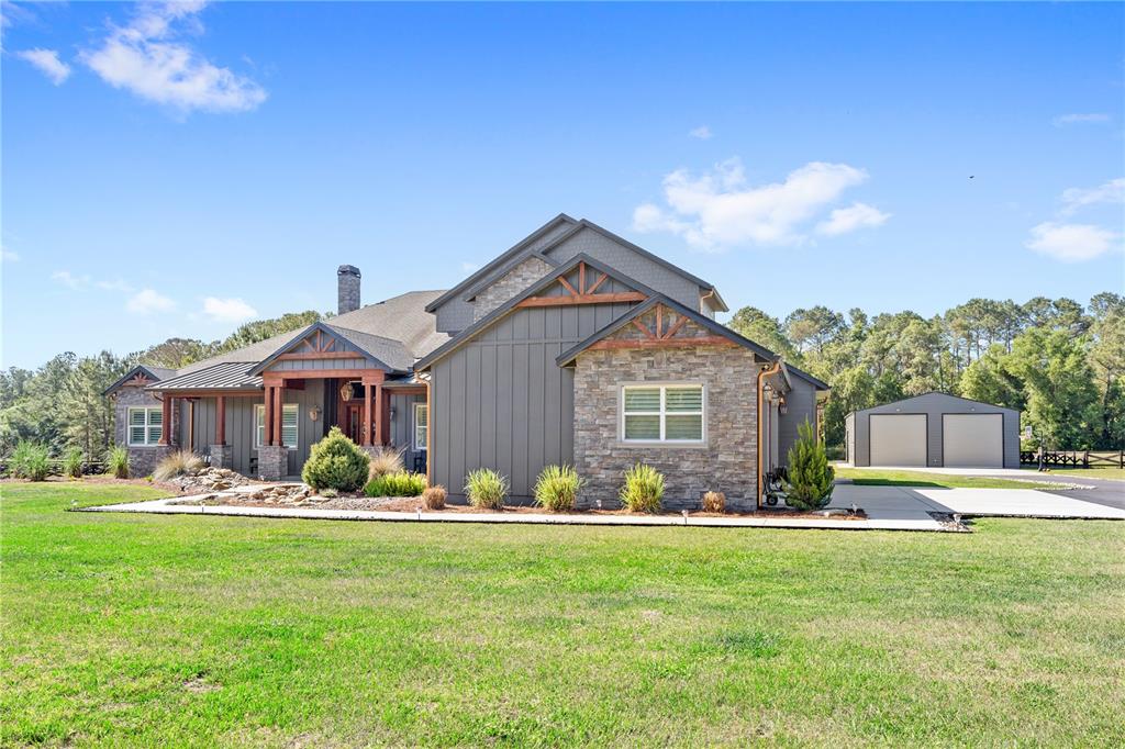 A gray house with stone accents and a detached garage sits on a grassy lawn — 22250 DEER PARK AVENUE, EUSTIS, FL