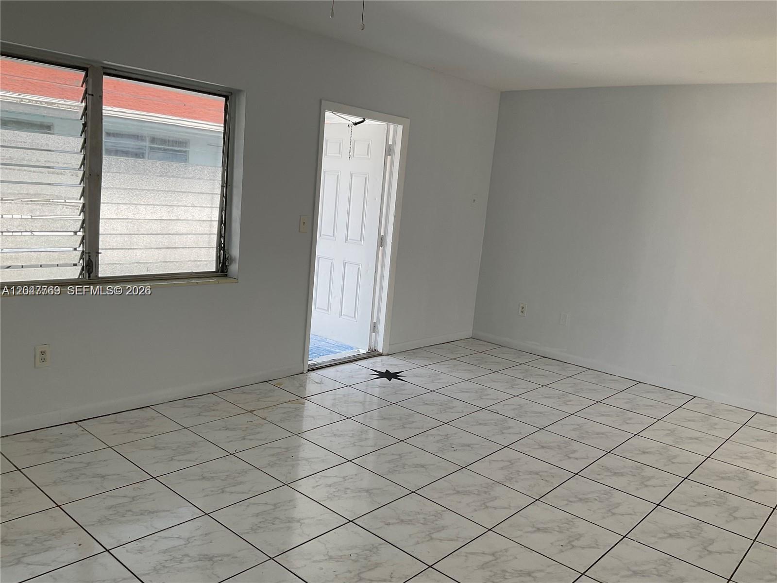 An empty room features white walls, white marble-patterned tile flooring, and a door leading outside — 1420 NE 171st St # 2, North Miami Beach FL 33162, NORTH MIAMI BEACH, FL