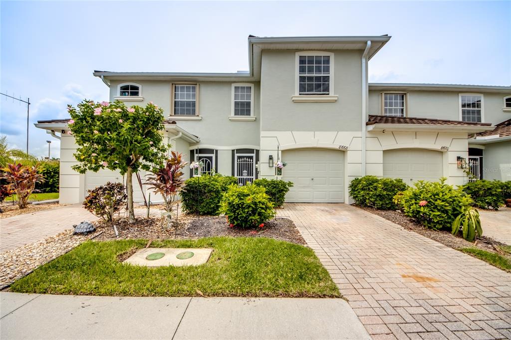 A two-story townhouse with a light-colored stucco exterior, two garages, and a paved driveway — 8668 ATHENA COURT, LEHIGH ACRES, FL