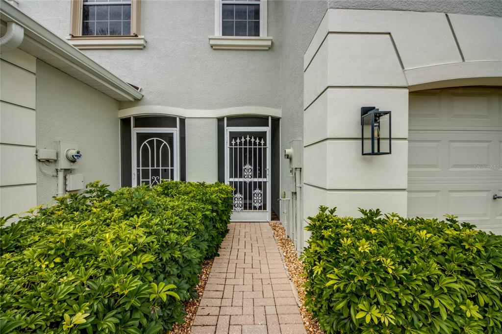A paved walkway leads to the front entrance of a home with two screen doors — 8668 ATHENA COURT, LEHIGH ACRES, FL