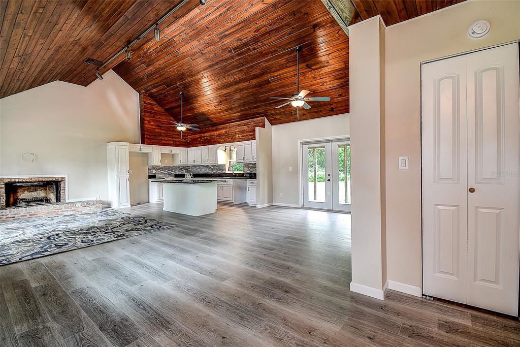 An open-concept living area features a vaulted wood-plank ceiling, a brick fireplace, and a kitchen — 11700 VALLEY ROAD, DADE CITY, FL