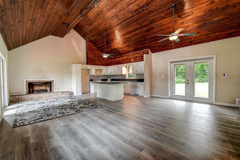 An open-concept living room and kitchen with a vaulted wood ceiling and brick fireplace — 11700 VALLEY ROAD, DADE CITY, FL